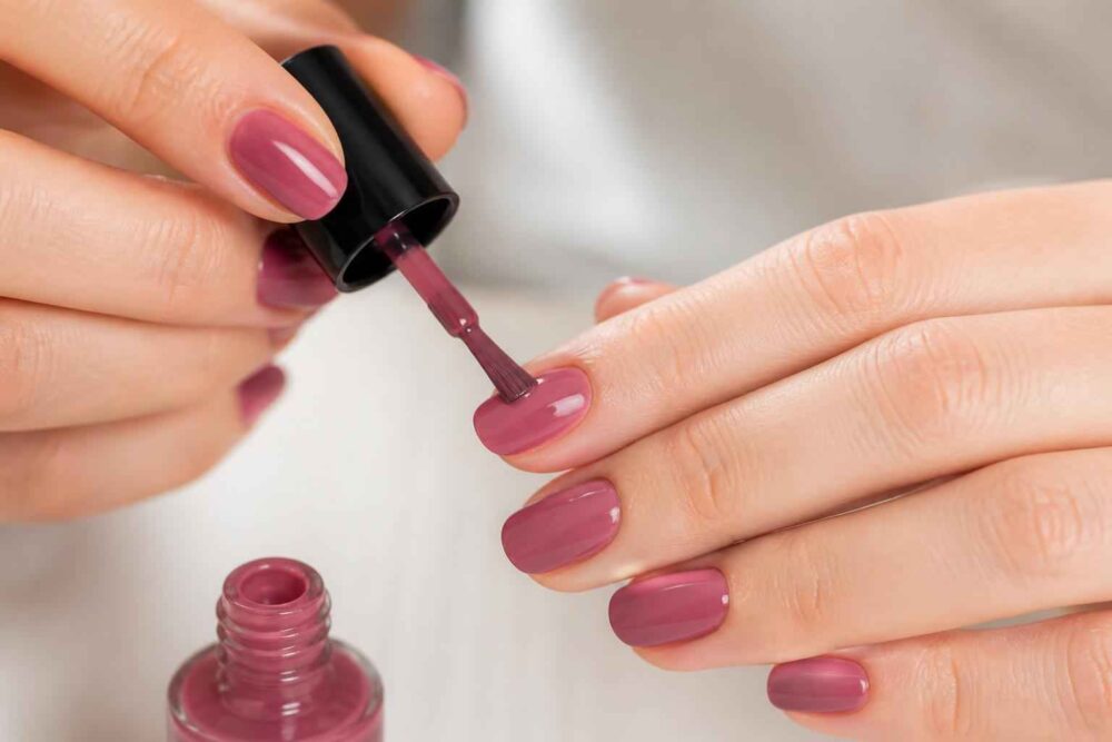 Kobieta nakłada różowy lakier na paznokieć pędzelkiem do manicure