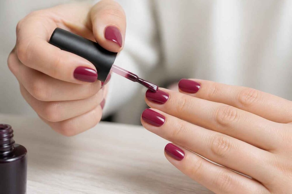 Kobieta maluje paznokieć bordowym lakierem przy użyciu pędzelka do manicure